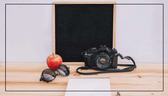 A vintage camera placed beside an apple, sunglasses, and a notepad on a wooden table, framed using the Rule of Thirds.