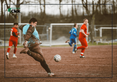 Mud-covered goalkeeper kicking the ball during an intense football match on a muddy field.