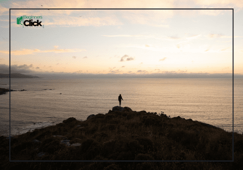 Silhouette of a person standing on a cliff during sunset overlooking the calm sea.