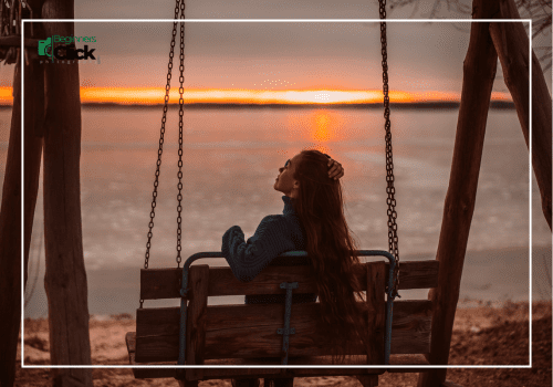 Woman sitting on a swing by the lake, enjoying a peaceful sunset view.
