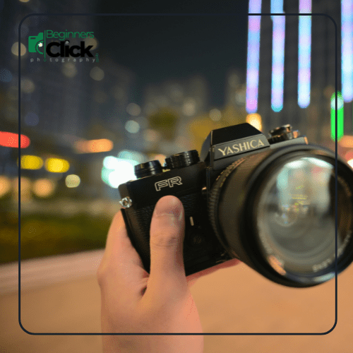Focusing Distance Demonstrated with Yashica FR Camera A hand holding a Yashica FR camera with a blurred city lights background, demonstrating focusing distance and shallow depth of field.