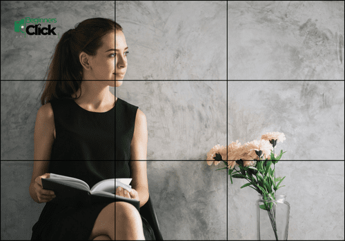 Rule of Thirds: Storytelling through Minimalist Portraits A young woman in a black dress holding a book sits beside a vase of white flowers, looking toward the light, positioned along the left third of the frame.