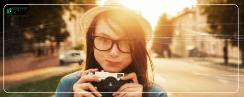Young Photographer at Sunset – Street Photography Mood Young woman with glasses holding a camera outdoors in warm sunset light.